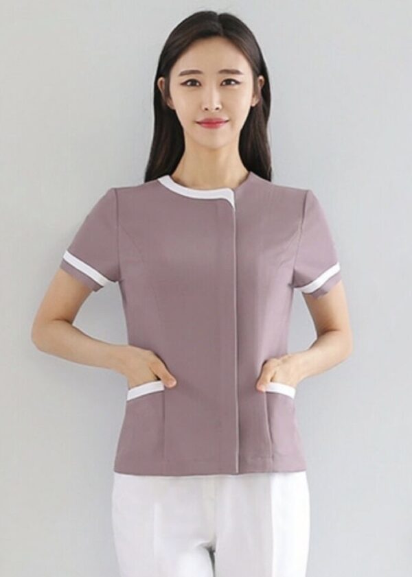 Dusty pink spa uniform with white piping, round neckline, and front pocket detailing